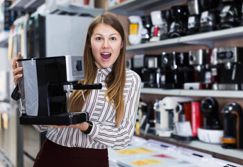 Portrait of delighted young woman with purchase in household appliances shop