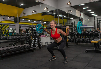 Young slim fit woman practicing squats with a barbell on her shoulders in a modern gym