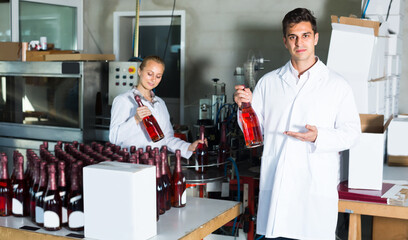 Fototapeta na wymiar Two young colleagues holding newly produced bottles of wine on winery manufactory