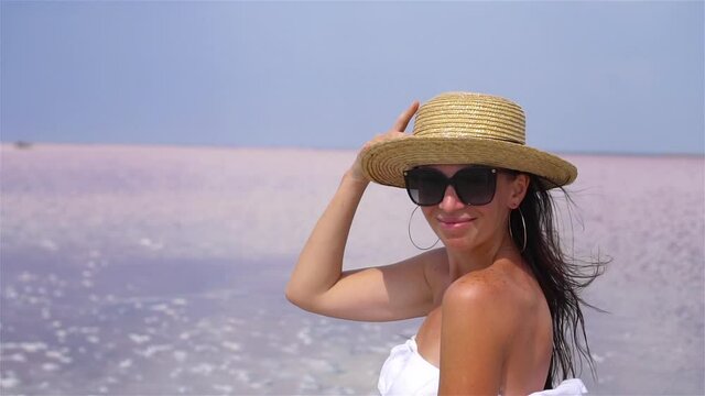 Woman in hat walk on a pink salt lake on a sunny summer day.