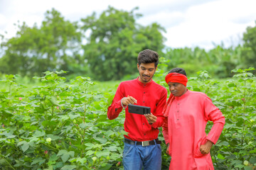 Young Indian farmer with agronomist at Cotton field , showing some information on tab