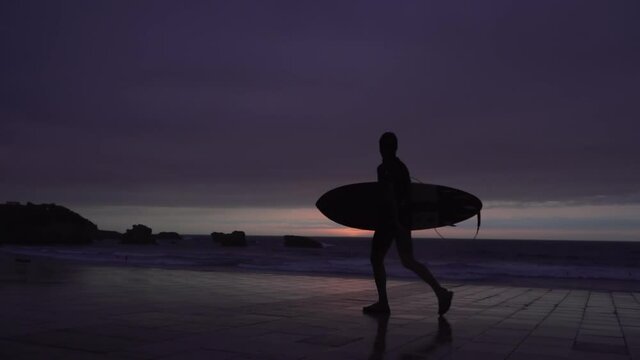 Surfer walking in front of the ocean with his board at sunset