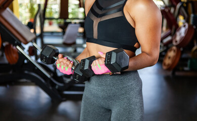 Fototapeta premium Sport Woman trains biceps with dumbbells in her hands in the gym