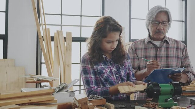 Grandfather and granddaughter are training woodwork Happy family activities within home. Senior carpenter is teaching and apprentice  young girl In wood factory. Concept Education and career