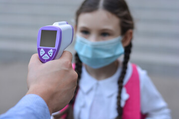 Temperature check in school . Child in medical mask in class in covid-19 outbreak.Teacher with thermometer at preschool or school entrance. Social distancing. Coronavirus prevention.