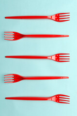 Vertical image.Top view of row of red plastic forks on the bright blue surface