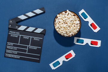 Movie clapper board, popcorn bowl and 3d glasses on classic blue background with deep shadows....
