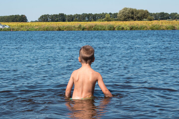 a boy stands in the water against the background of a yellow field