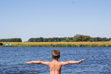 boy stands in the river against the background of a yellow field