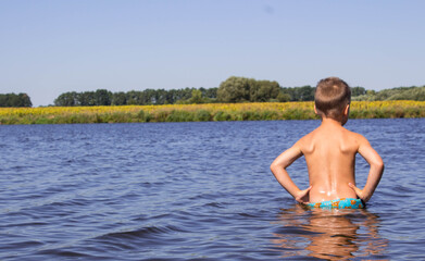the boy stands in the river and looks at the yellow field