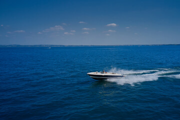 Aerial view of a boat in motion on blue water. In the background coastline