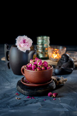 brown ceramic Cup of rosebud tea sits on a wooden table. Tea time, cozy atmosphere. Kitchen still life with tea from pink flowers with warm light in the background