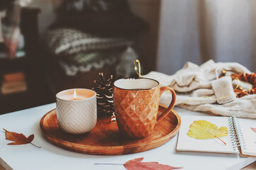 cozy autumn or winter morning at home. Still life details with cup of tea, candle, sketch book with herbarium and warm sweater. Scandinavian hygge concept