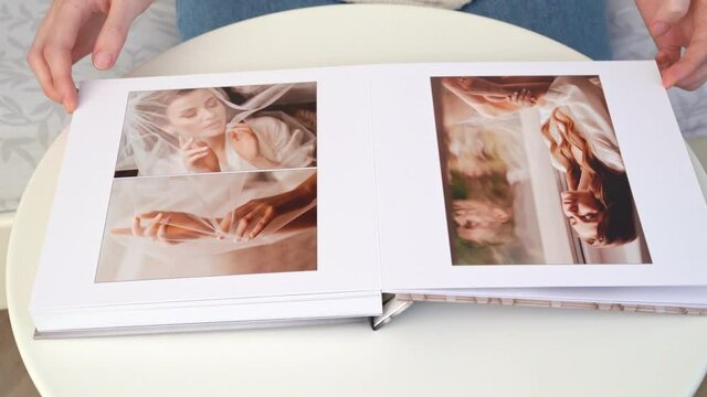 flipping through wedding photo book with thick pages on white table.