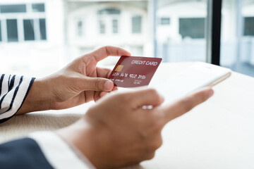 The businesswoman's hand is holding a credit card and using a smartphone for online shopping and internet payment in the office