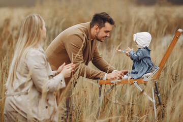 Family in a autumn field. Lady drawing. Man in a brown coat.