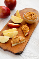 Raw Red Apples and Peanut Butter on a rustic wooden board on a white wooden background, low angle view.