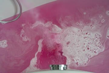 Bathtub with pink bath water and white foam