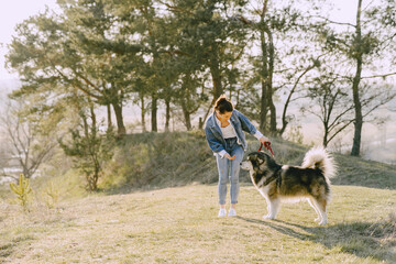 Woman in a spring forest. Girl with cute dog. Brunette in a jeans jacket.