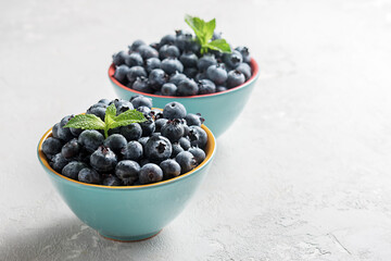 Fresh blueberries in bowls on a concrete surface with a copy of space.