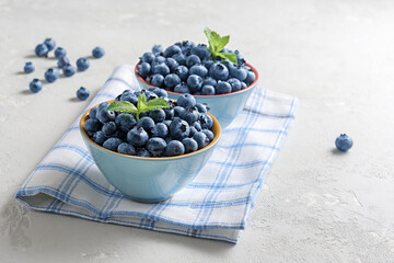 Fresh blueberries in bowls on a concrete surface with a copy of space.