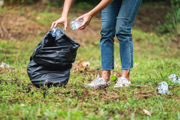 Closeup image of a female activist picking up garbage plastic bottles into a plastic bag in the...