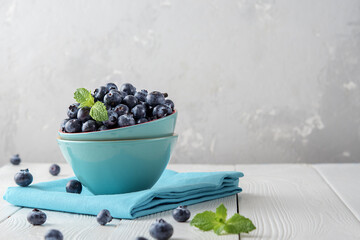 Fresh blueberries in a blue bowl on a light wooden table with copies of space.