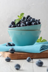 Fresh blueberries in a blue bowl on a light wooden table.