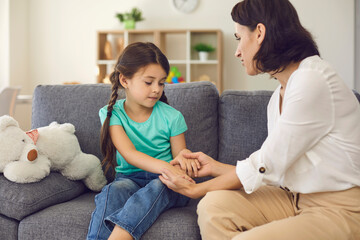 Mother sitting with daughter, holding her hands, talking to her and teaching her something