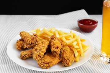 Homemade Crispy Chicken Wings and French Fries on a white plate, glass of cold beer, side view. Close-up.