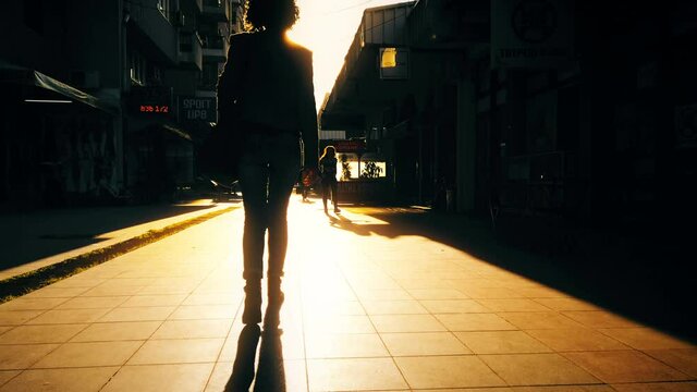 Silhouette woman walk on pavement in modern city during vibrant sunrise