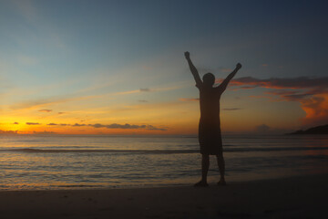 Fototapeta na wymiar A man raising arms at sunset seaside beach Success, celebrating goals and achievement.