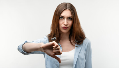 Fototapeta premium Photo of Beautiful girl in casual clothes, looking is upset at the camera, holding thumb down. Concept of dislike