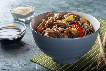 Wok with soba noodles. Buckwheat soba noodles in a grey Cup with chopsticks. Soba noodles with chicken, celery and red sweet pepper.