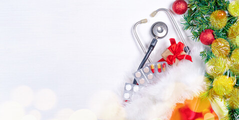 Medical banner with pills, gift present box, stethoscope and Christmas tree on white wooden background. Copyspace. Medicine new year flatly.