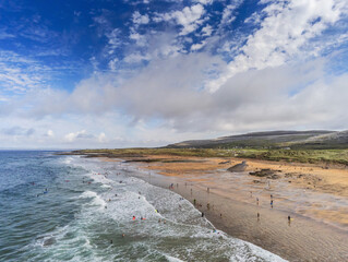 Aerial drone view on Fanore beach, county Clare, Ireland. Warm sunny day, People on the beach and surfing in the water. Cloudy sky, Popular surfing spot.