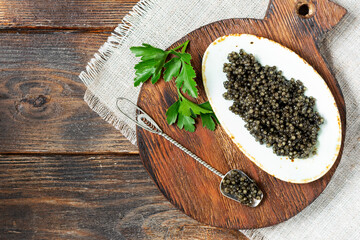 Obraz na płótnie Canvas Black caviar. Black sturgeon caviar in a ceramic bowl and in a metal spoon on a wooden serving Board. A healthy treat. Top view with space for text