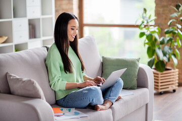 Full body photo of smart asian manager girl sit divan legs crossed folded work remote use laptop prepare coach boss report wear denim jeans in house indoors