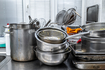Dirty pots and pans piled up for washing in restaurant kitchen.