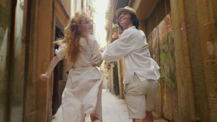 Fototapeta premium Close up happy couple running away on old city. Cute man and woman having fun
