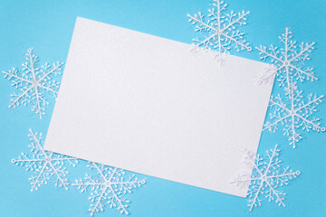 White sheet of paper on a blue background in the center, white snowflakes around the sheet. Empty space for entries.The view from the top
