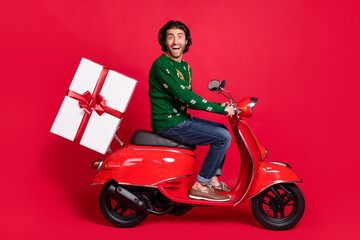 Fototapeta na wymiar Profile side view portrait of his he attractive glad amazed cheerful cheery guy riding moped delivering big large giftbox December winter isolated bright vivid shine vibrant red color background