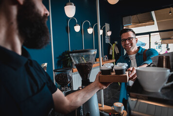 Men in coffee shop buying cappuccino in plastic cup from barista.