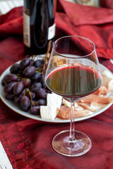Wino czerwone i kieliszek .Talerz z prosciutto, serem brie i gorgonzolą, orzechami greckimi i winogronem.