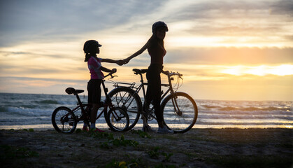 Silhouette Lovely family raise give me five at sunset for relax and freedom. Mom and daughter bicycling at the beach. Lifestyle Concept.