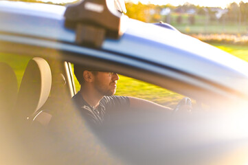 portrait of attractive nerd in long sleeve glasses and beard in the electric car at sunset