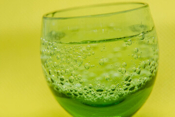 Closeup small green glass cup with bubbly water on a yellow background.