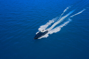 Obraz premium Speed boat movement at high speed aerial view. High-speed yacht of blue color fast motion on blue water in the rays of the sun top view.