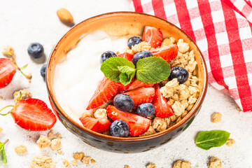 Greek yogurt granola with fresh berries on white stone table.