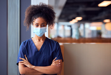Female Doctor In Face Mask Wearing Scrubs Under Pressure In Busy Hospital During Health Pandemic - Powered by Adobe